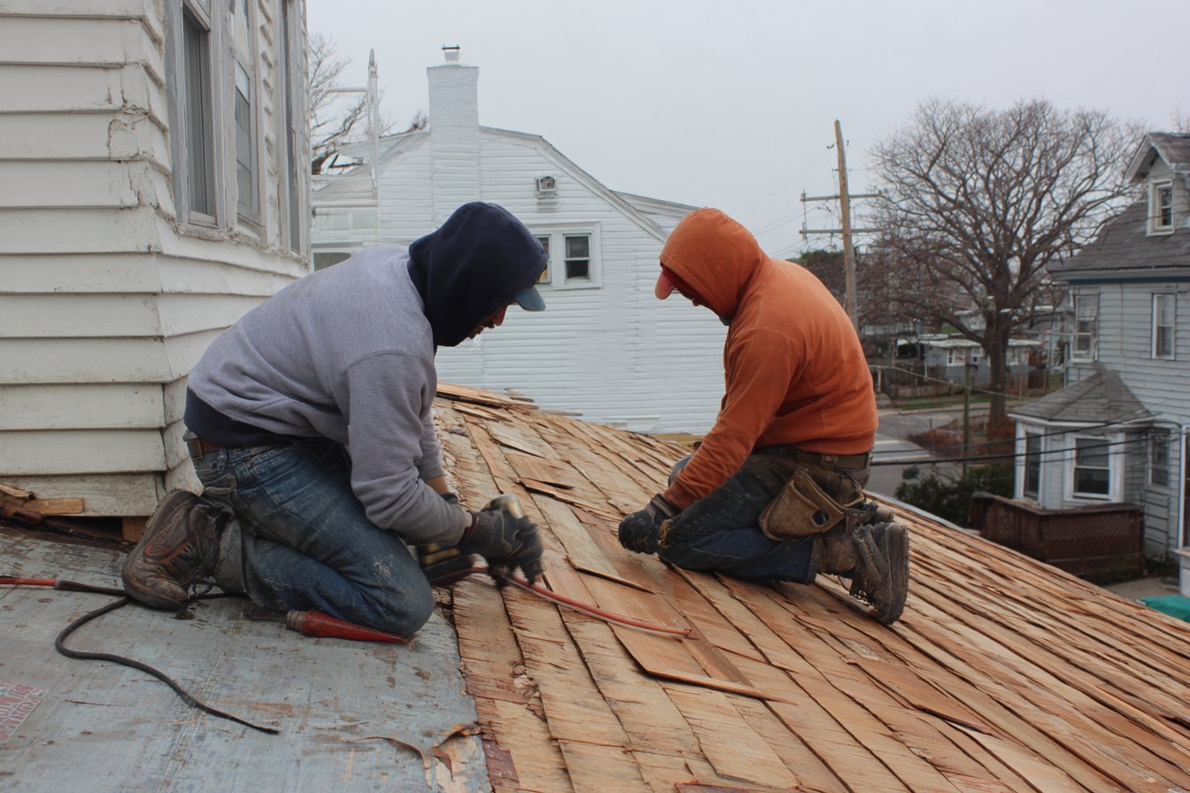 Flat Roofers NY crew nailing new tapersawn red cedar shakes onto a Queens colonial roof after the old shakes were torn off