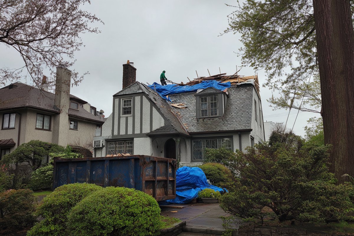Blue tarps covering the yard and plantings of a Queens Tudor while the crew tears old cedar shakes off the roof into a dumpster