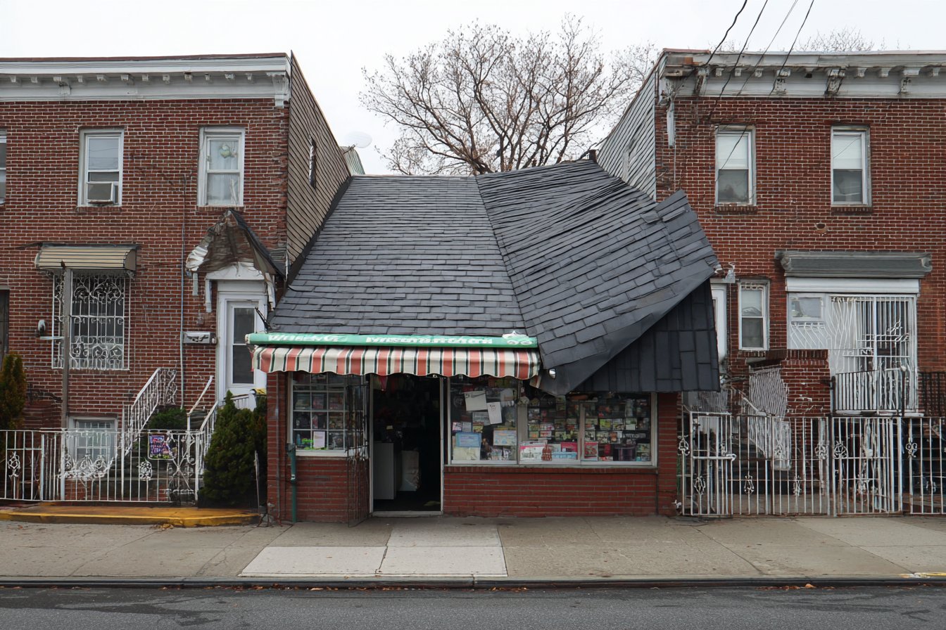 New charcoal architectural shingles on the steep-slope roof of a Queens storefront building, with the shop open below