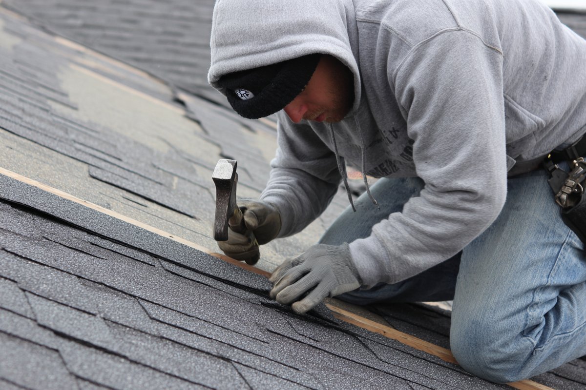 Roofer hand-nailing an architectural shingle along the manufacturer's nail line