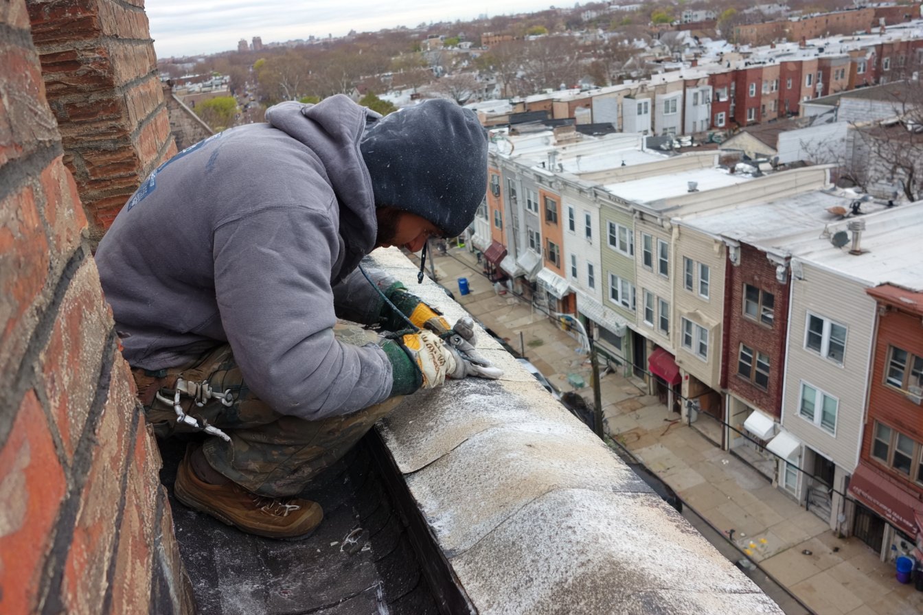 Roofer sealing a leaking crack in the concrete slab roof of a Queens apartment building, beside the parapet wall