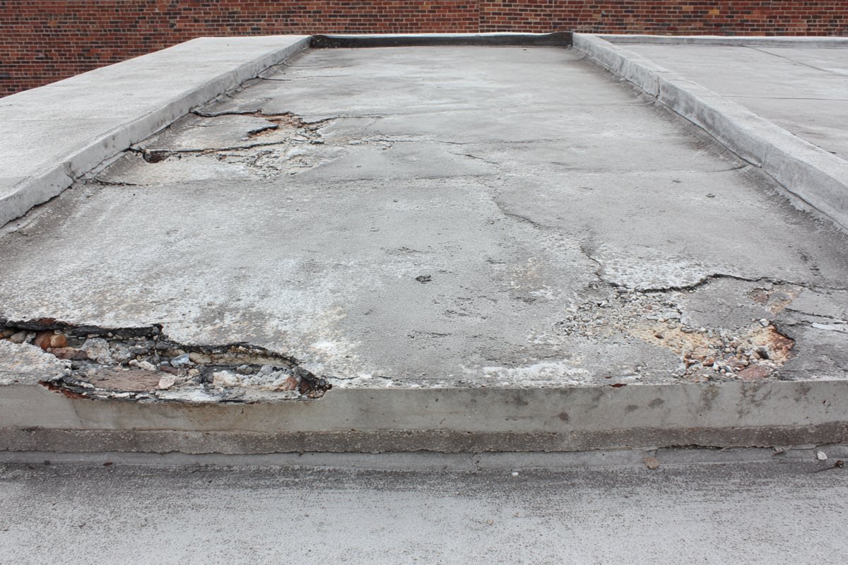 Unprotected concrete roof slab with spalled patches and exposed, rusting rebar