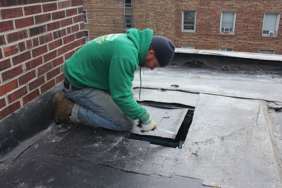 Roofer cutting out a section of flat roof membrane to expose waterlogged insulation board on a Queens apartment building