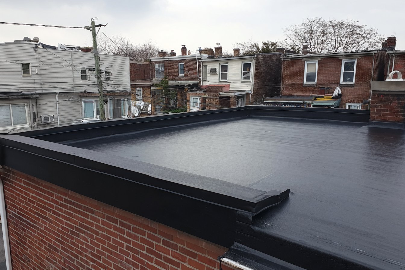 Newly installed black EPDM rubber membrane covering a Queens row house flat roof, seams and parapet flashing finished