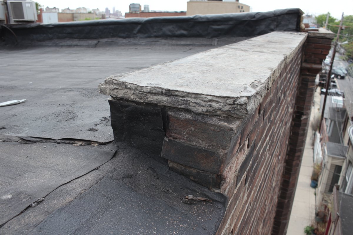 Aging black EPDM roof with a separated seam and shrinkage pulling the membrane back from a parapet