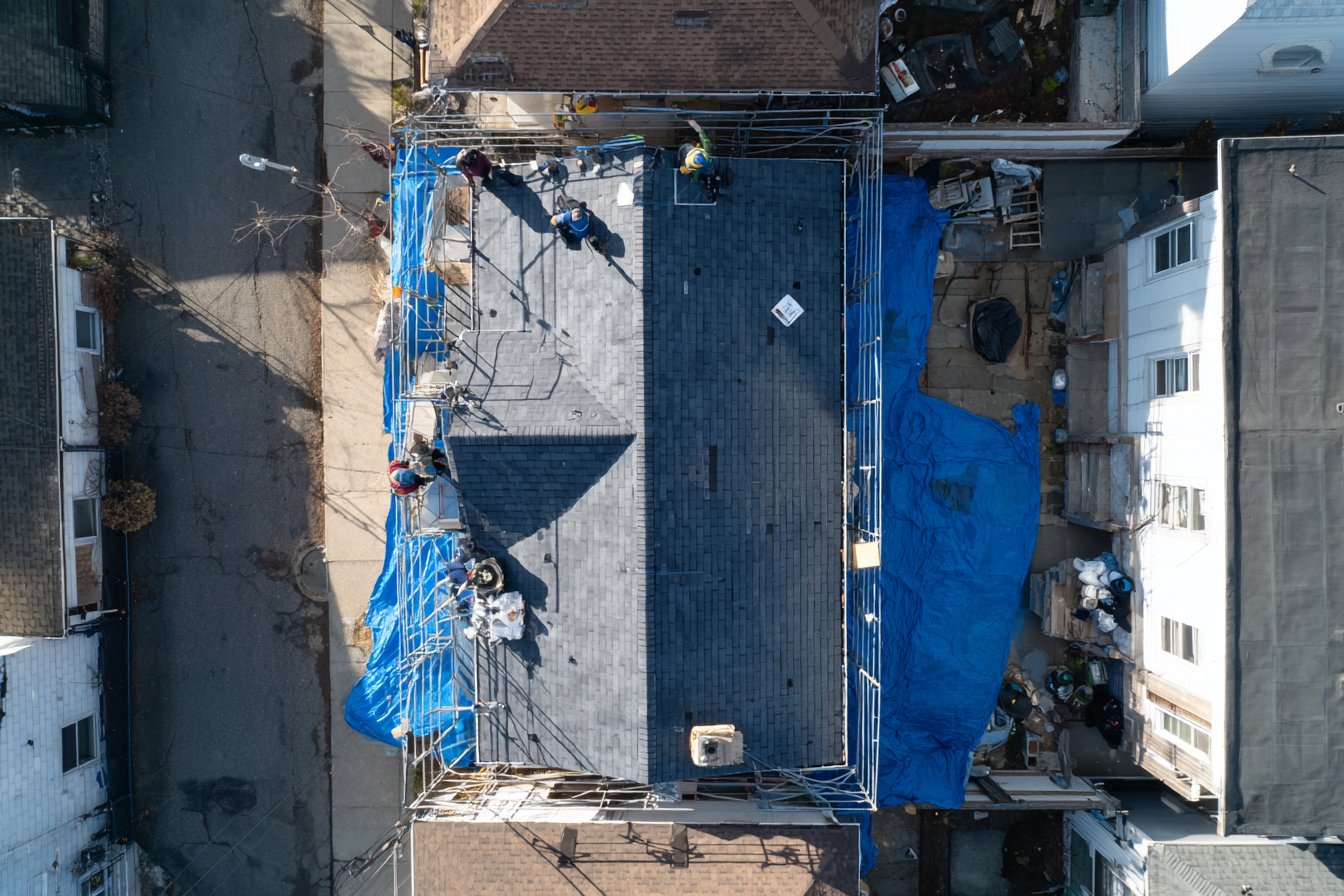 Finished flat concrete tile roof in charcoal on a Queens two-family home, with a clean ridge line