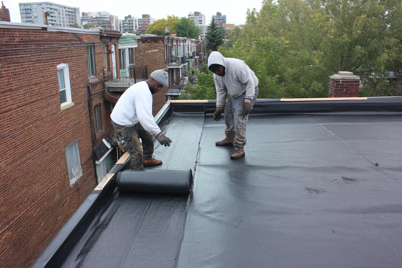 Flat Roofers NY crew unrolling a new black EPDM rubber membrane across a Queens rowhouse flat roof