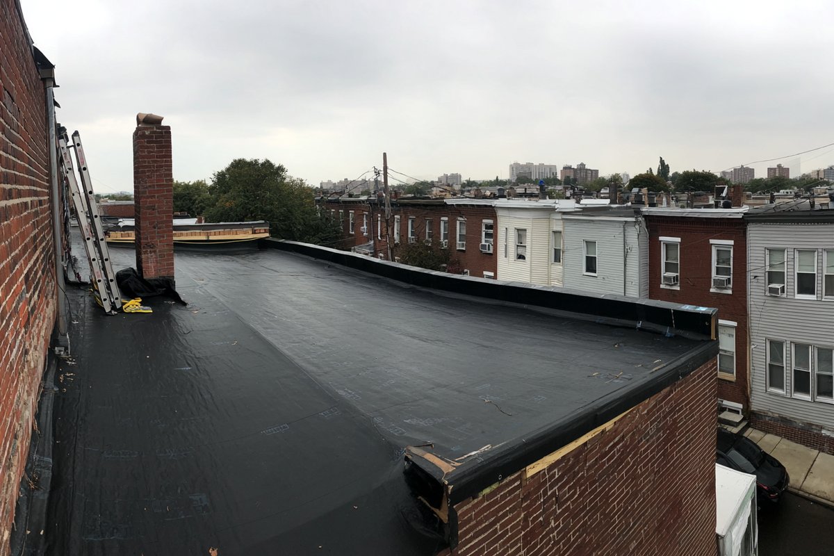Finished black EPDM roof on a Queens multi-family building, wide sheets with few seams running to the parapet