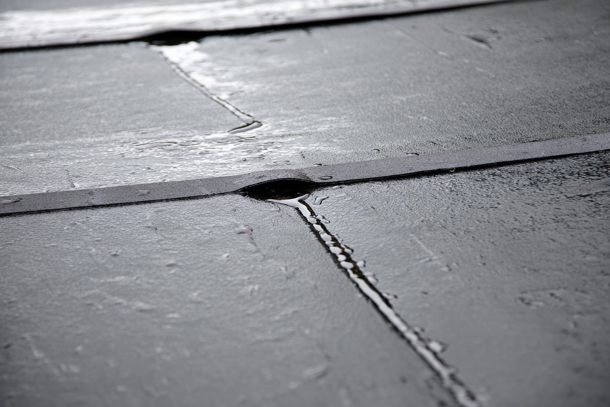 Close-up of a taped EPDM seam on a new rubber roof after rain, water running toward the drain