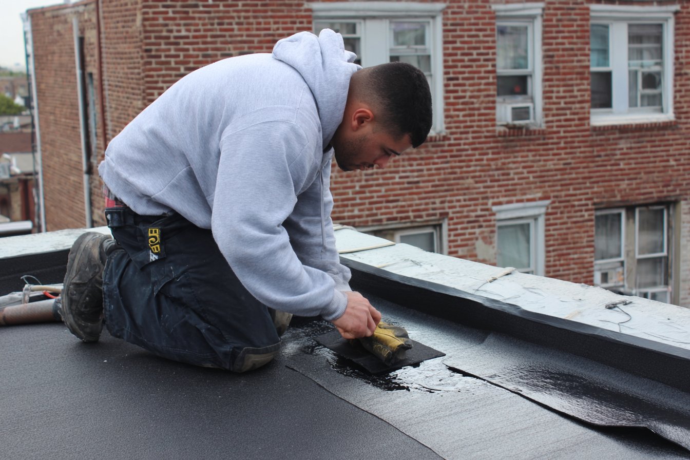 Flat Roofers NY roofer sealing a patch over a leak on a flat EPDM roof of a Queens rowhouse