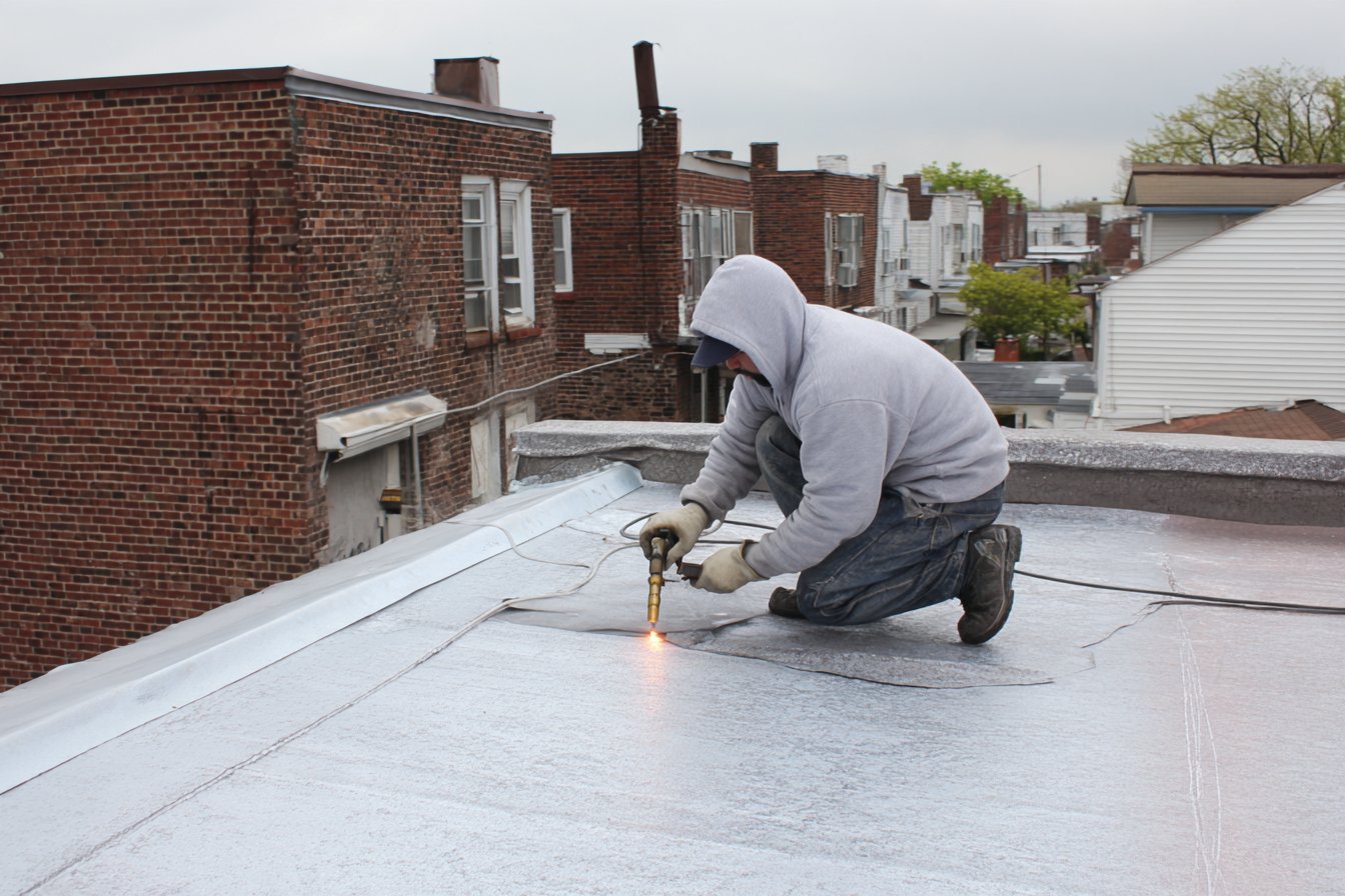 Roofer heat-welding a membrane patch over a torn seam on a Queens flat roof