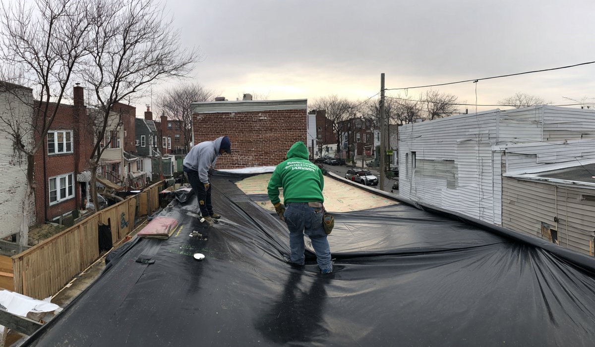 A crew laying a new membrane on a Queens flat roof