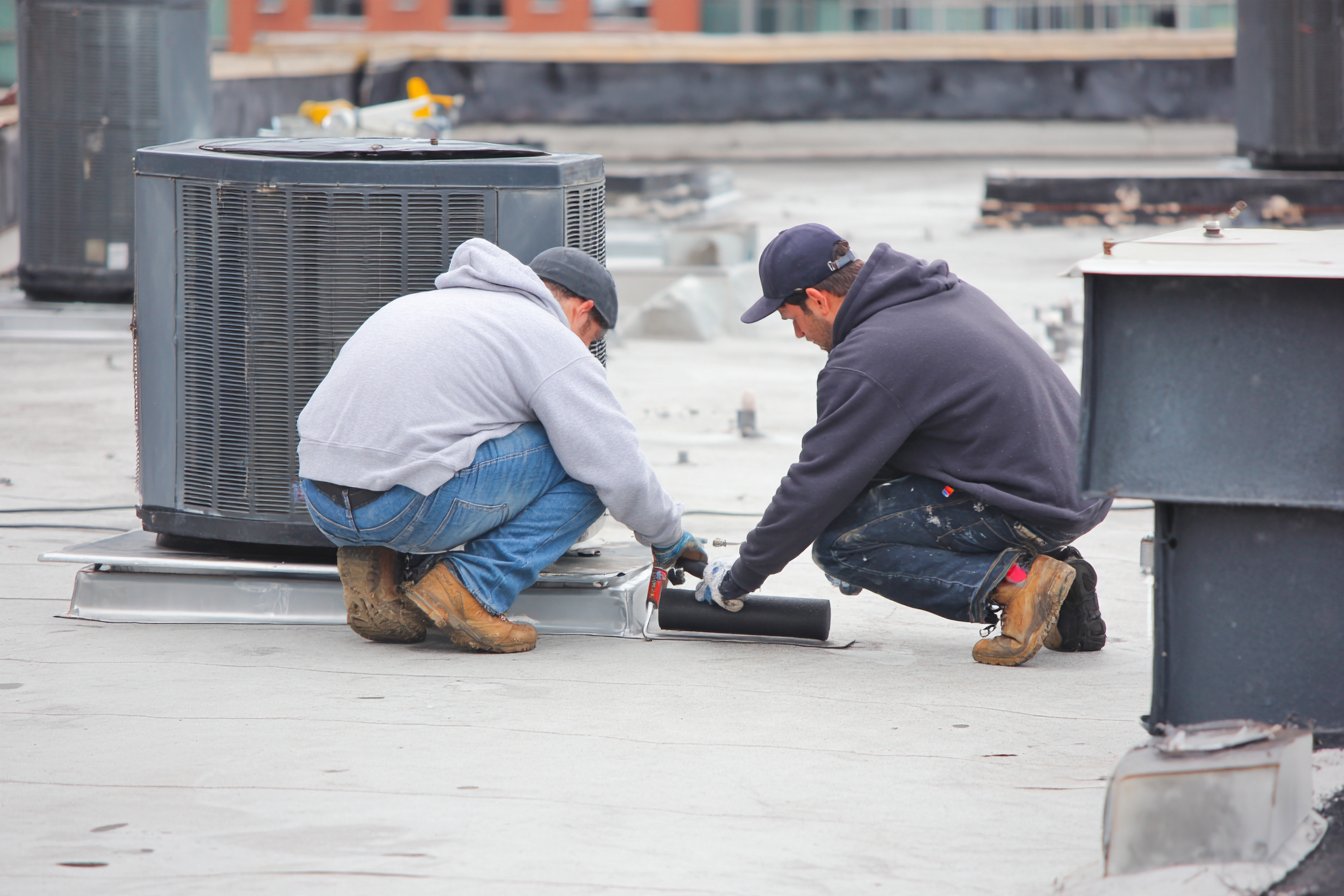 Flat Roofers NY crew sealing a TPO seam beside a rooftop HVAC unit on a Queens hotel roof