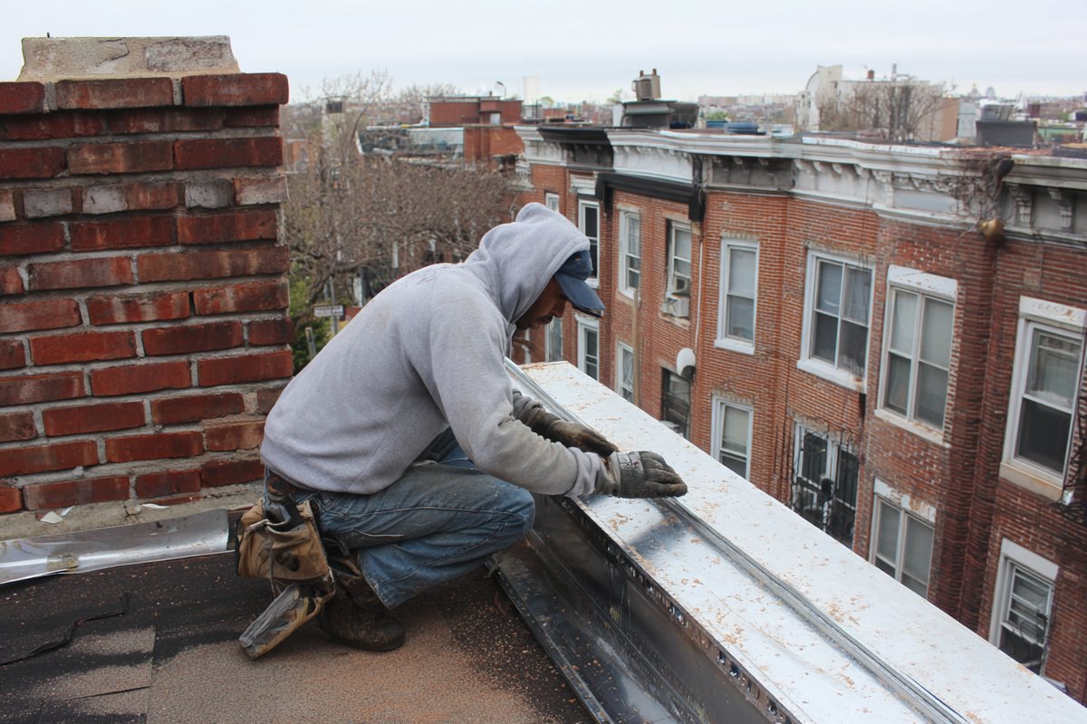 Roofer working a parapet edge on an upper story of a Queens row house