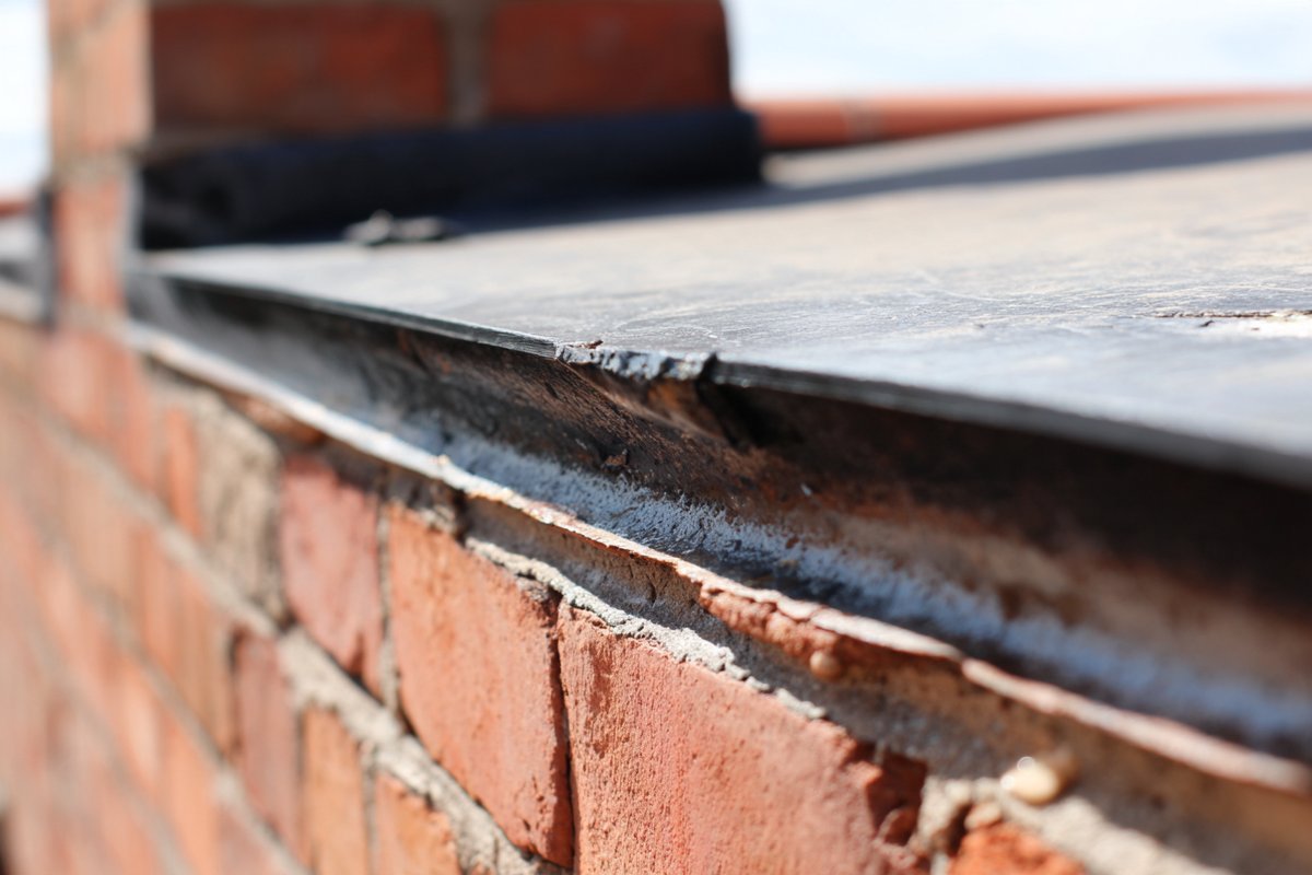 Close-up of lifted flashing where the flat roof membrane meets a brick parapet wall