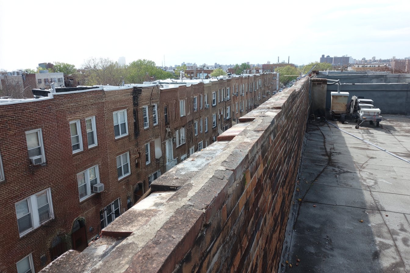 A block of attached brick row houses in Jamaica, Queens, their flat roofs running into one another behind a continuous parapet
