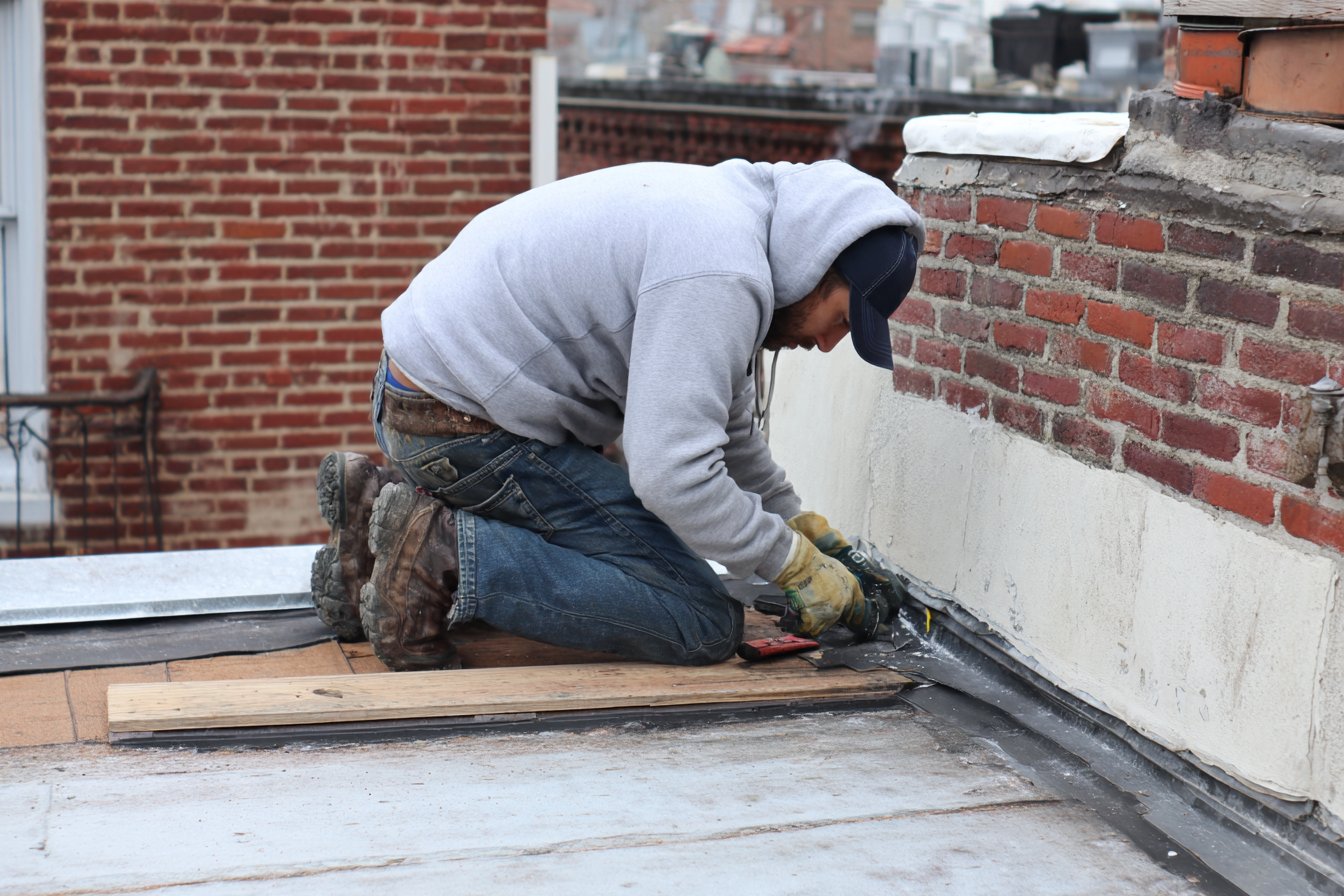 Flat Roofers NY roofer re-flashing the joint where the flat roof of a rear kitchen extension meets the brick back wall of a Queens row house