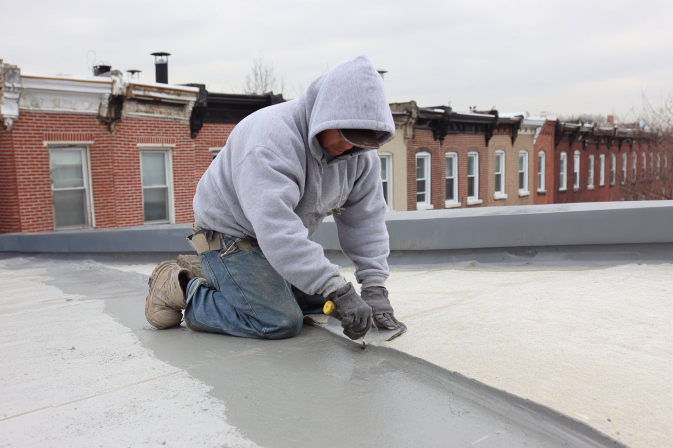 Roofing crew resealing a seam on the low-slope roof of a rear extension in Queens