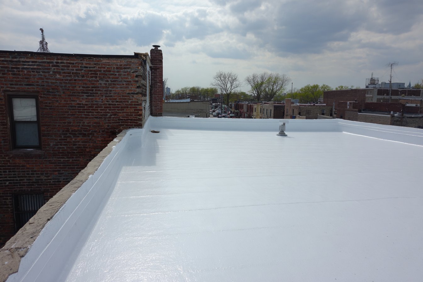 Finished white TPO flat roof on a Queens row house, seams welded and parapet flashing complete