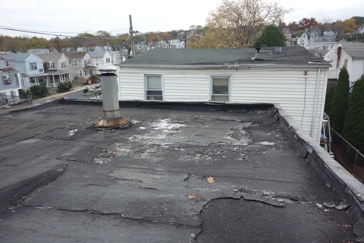Before: worn, patched flat roof on the same Jamaica home before the tear-off