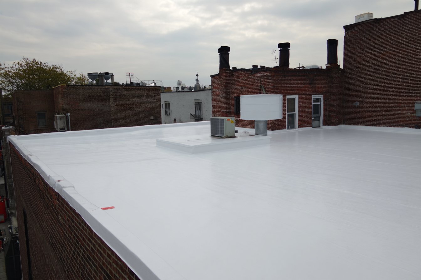 New white TPO membrane on the finished flat roof of a mixed-use building in Corona, Queens