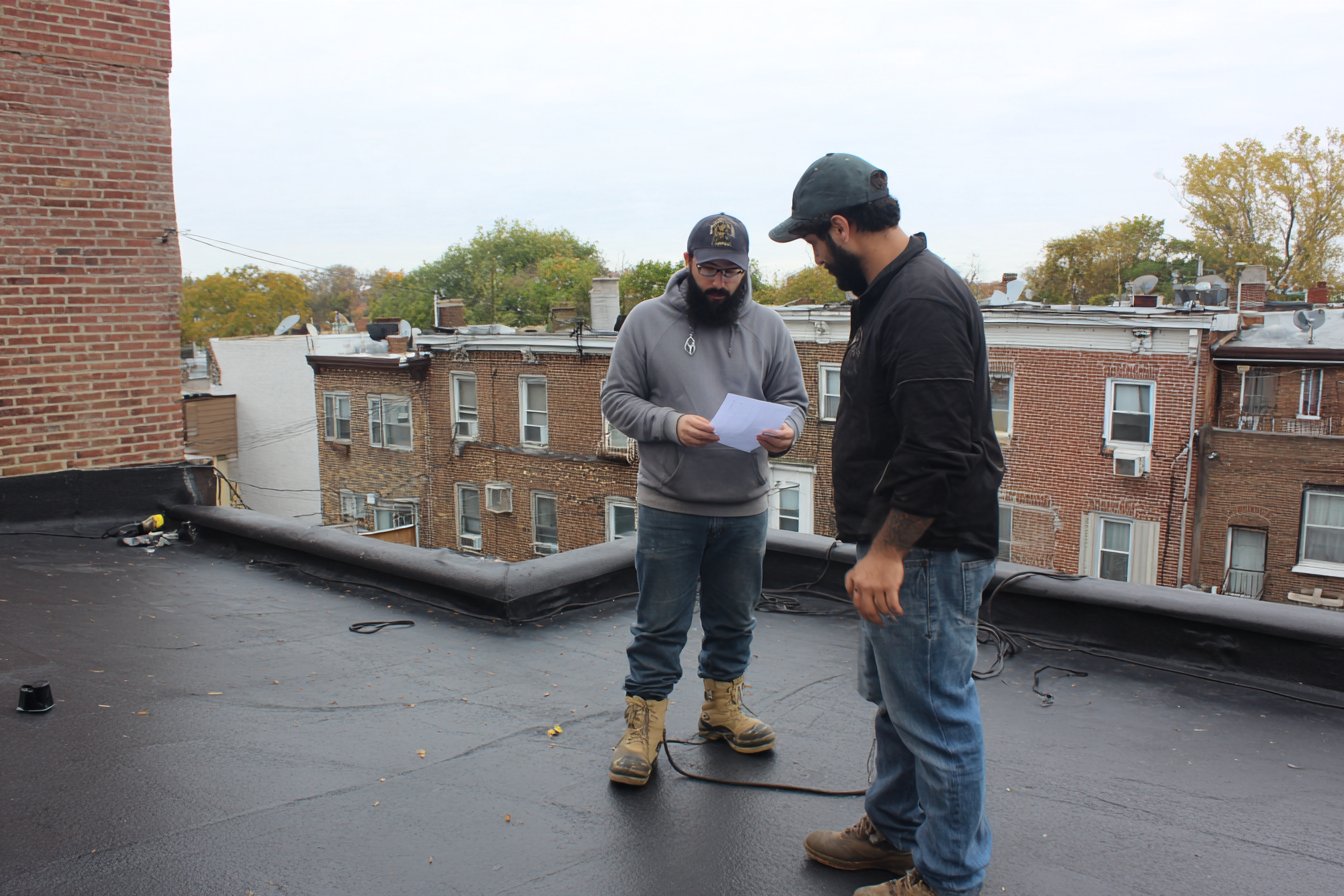 Flat Roofers NY estimator walking a Queens rowhouse flat roof with the owner, going over a written estimate