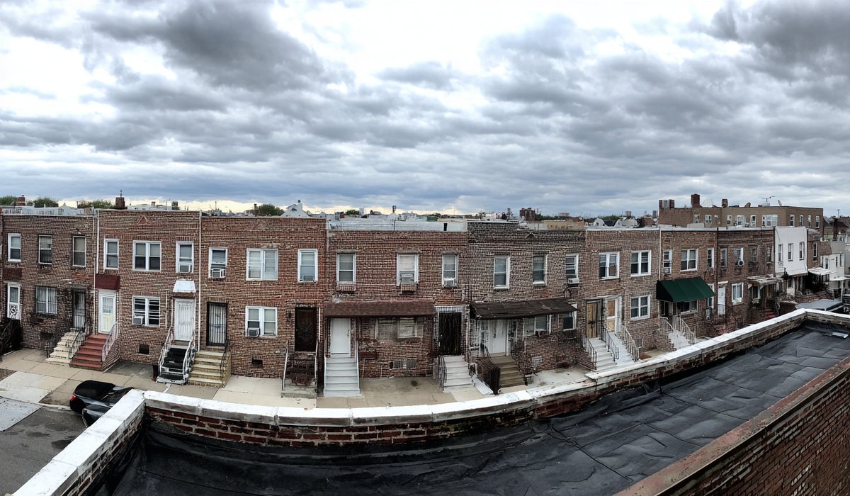 Row of attached two-family brick homes in Rockaway Beach with flat modified bitumen roofs divided by a shared parapet wall