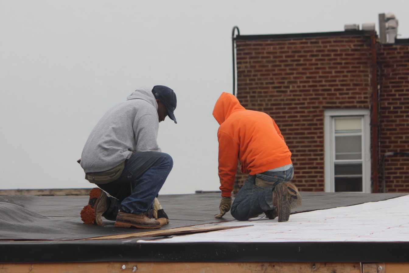 Flat Roofers NY crew rolling out a new black EPDM rubber membrane over fresh insulation board on a torn-off Queens rowhouse flat roof