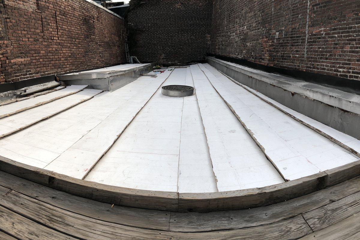Tapered insulation boards laid toward a new roof drain on an opened-up Queens flat roof, before the new EPDM goes down