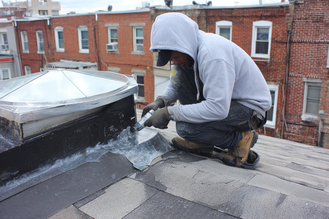 Flat Roofers NY roofer resealing the flashing around a curb-mounted dome skylight on a Queens rowhouse flat roof