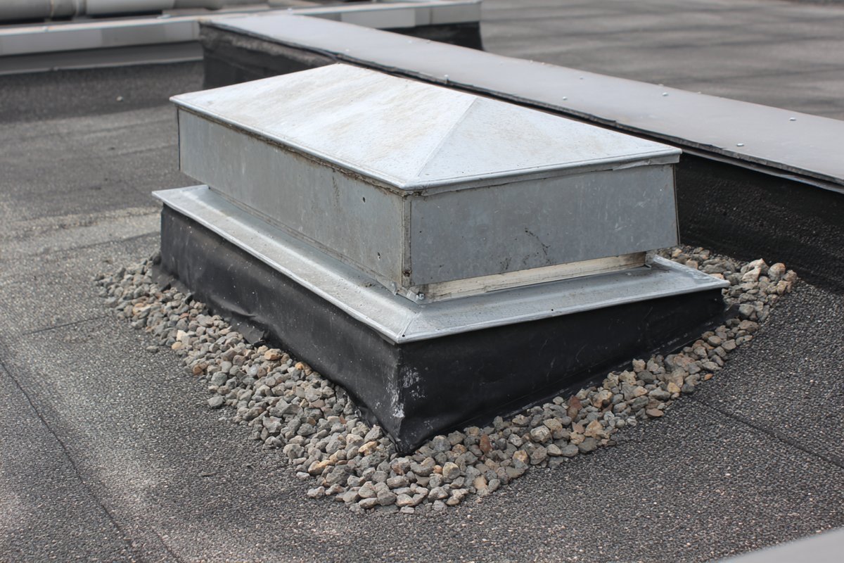 Curb-mounted skylight on a Queens flat roof, showing the metal curb flashing and the roof membrane turned up the sides of the curb